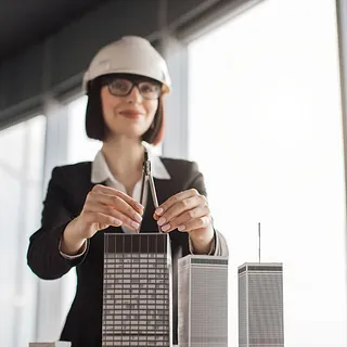 arquitecta con casco de seguridad posa junto a maqueta de edificios