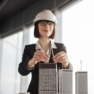 arquitecta con casco de seguridad posa junto a maqueta de edificios